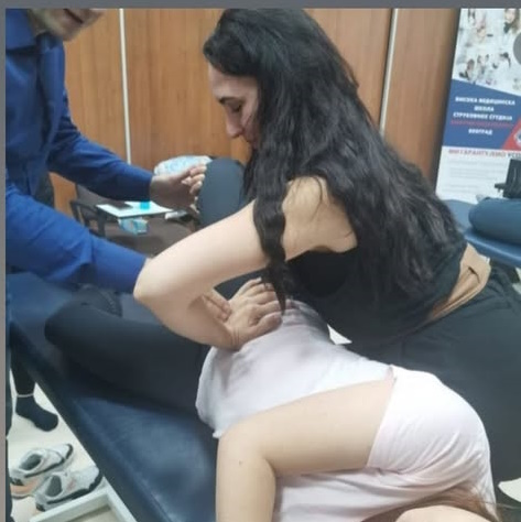 Dva terapeuta primenjuju spiralnu stabilizaciju na pacijentu u bočnom položaju, stabilizujući karlicu i aktivirajući mišiće trupa kroz manuelnu korekciju
