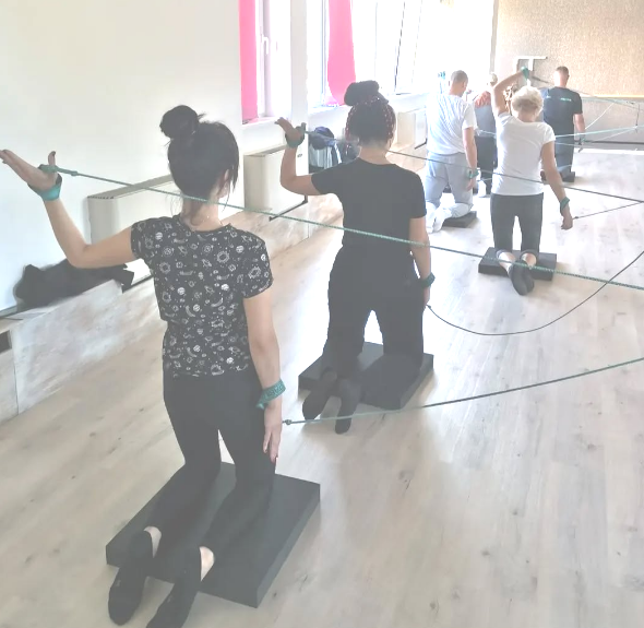 Grupna vežba spiralne stabilizacije sa trakama, fokusirana na korekciju posture i aktivaciju mišića leđa